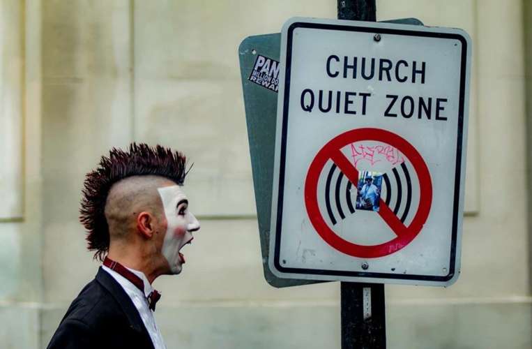 A man with a face painted as mime standing next to the sign with information church quiet zone