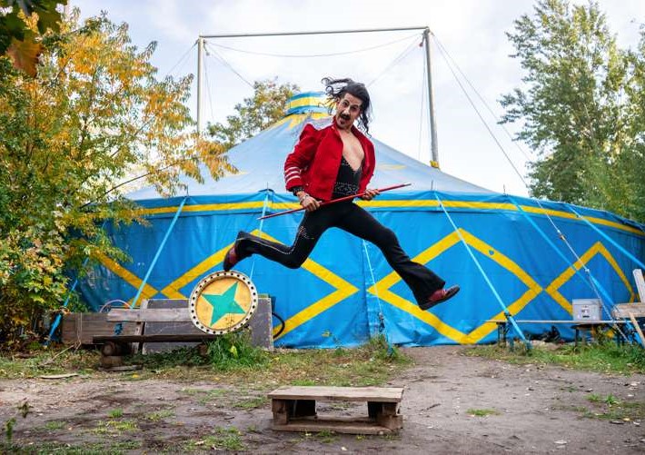 A man jumps in front of a blue circus ten